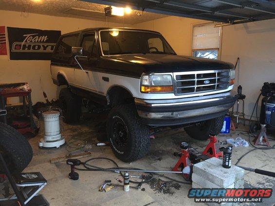 Lifted black and white 1994 Ford Bronco in a garage with front end raised on jacks