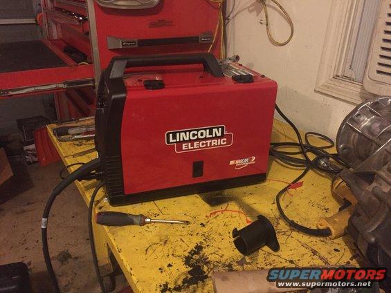 Red Lincoln Electric welder with NASCAR Performance sticker on a yellow workbench