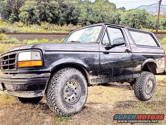 Black 1995 Ford Bronco parked on dirt with trees and railroad tracks in background