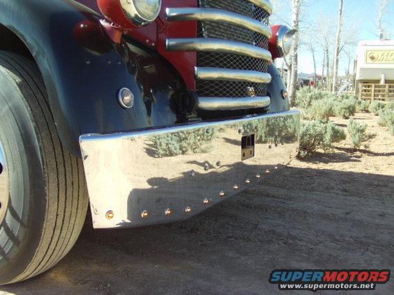 Chrome bumper with amber marker lights and a large grille with horizontal bars on a dark red and black truck