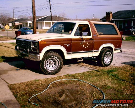 Brown and white Ford Bronco parked on a driveway. Some rust spots on the side