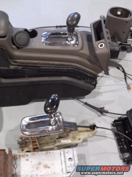 Two car center consoles with gear shifters and wiring, one above the other