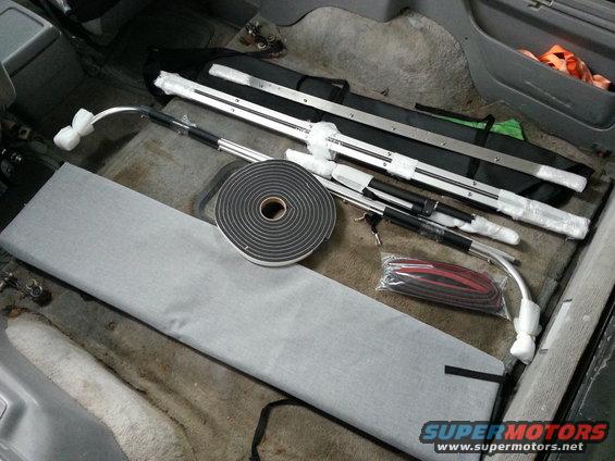 Interior of a vehicle with parts and supplies laid out on the floor, including metal bars, foam tape, and wiring