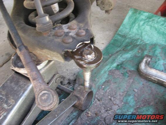 Close-up of a damaged suspension component, possibly a ball joint, with a jack and tools nearby