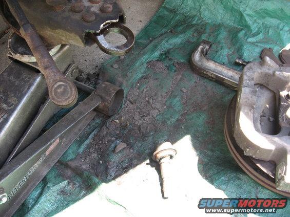 Automotive parts and tools on a green tarp, including a jack, tie rod ends, and a brake rotor