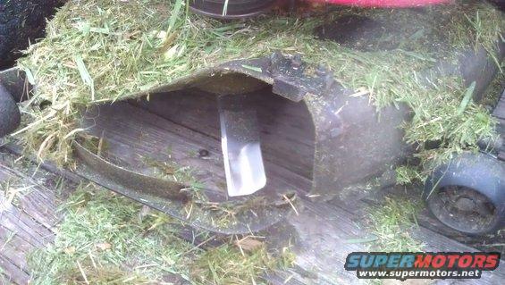 Close-up of a lawn mower deck showing the blade and grass clippings. Supermotors.net logo visible
