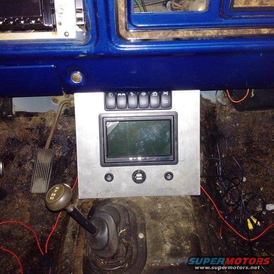 1978 Ford Bronco interior showing custom dashboard panel with toggle switches and a screen, plus floor shifter and pedals