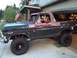 1978 Ford Bronco - A boy smiles from the driver's seat of a weathered 1978 Ford Bronco with a lifted suspension.
