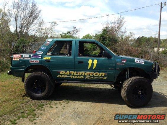 Green off-road vehicle with large tires and racing decals, side view