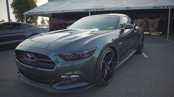 Dark green Ford Mustang parked, another Mustang in background. Nitto tent behind