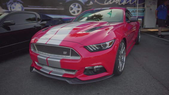 Red 2015 Ford Mustang GT with silver racing stripes parked next to a black car