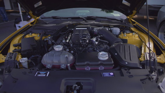 Yellow engine bay with a supercharged engine, black intake, and coolant reservoirs
