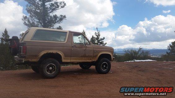 Brown 1980s Ford Bronco with a spare tire on the back, parked on a dirt hill