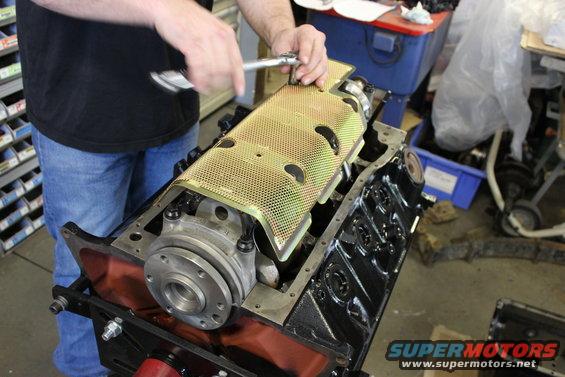 Engine block assembly with a yellow perforated cover being installed