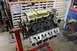 1979 Ford Bronco - Engine assembly on a stand in a workshop environment, with storage cabinets in the background.