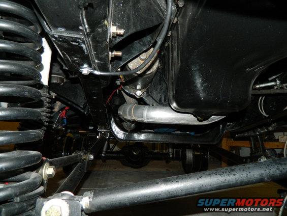Underside view of vehicle suspension, exhaust pipe, and differential. Supermotors.net logo visible