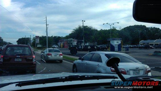 Cars in traffic on a road with buildings and trees in the background