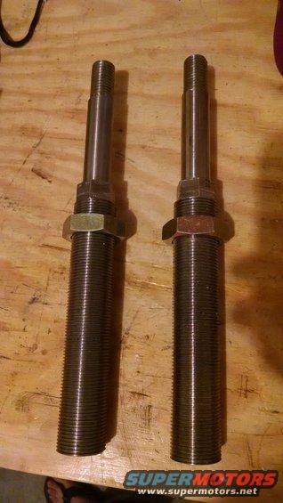 Two threaded metal shock absorber components with hex nuts on a wooden surface