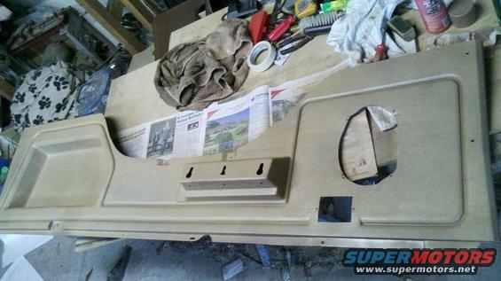 Tan interior door panel with a large circular cutout and a smaller rectangular cutout, lying flat on a workbench
