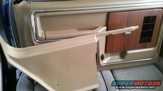 Tan car door panel with wood grain accent and chrome trim, showing a detached lower trim piece