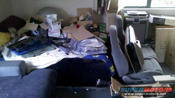 Car seats and disassembled parts piled in a cluttered room with boxes