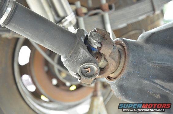 Drive shaft U-joint connected to a dark differential housing, with a rusty brake rotor visible