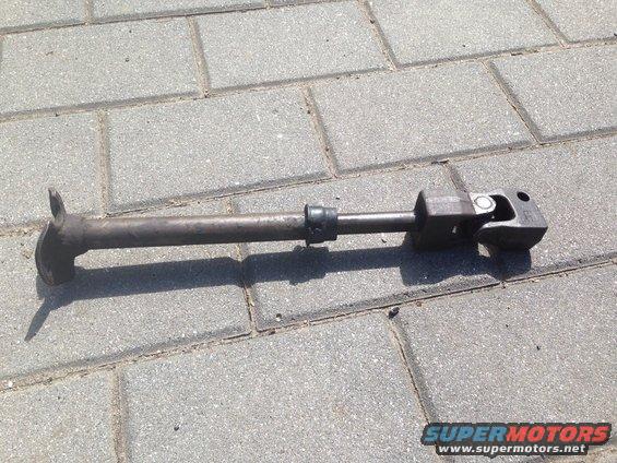 Steering shaft with two U-joints and a rubber boot, lying on a paved surface