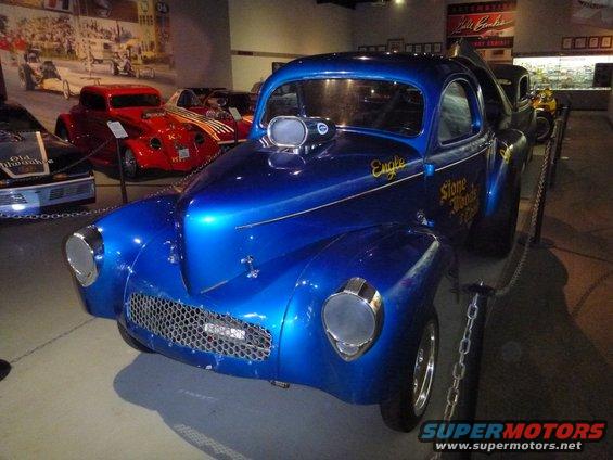 Blue hot rod with supercharger and 'Stone Woods & Cook' lettering on the side. Other cars visible in background