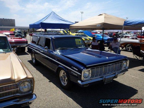 Dark blue station wagon with a roof rack parked at a car show. Other cars and tents are visible