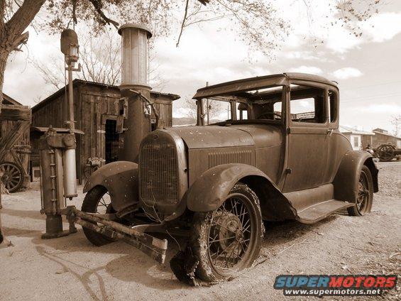 Brown 1928 coupe with flat tires at an old gas station
