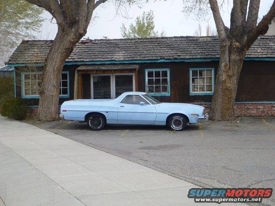 Light blue pickup truck parked next to a building with two large trees
