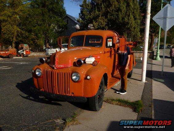 Orange fire truck parked on street, front view. A person stands next to it