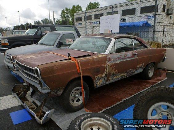 Rusty 1967 Ford Fairlane 500 with detached front bumper, parked next to other vehicles