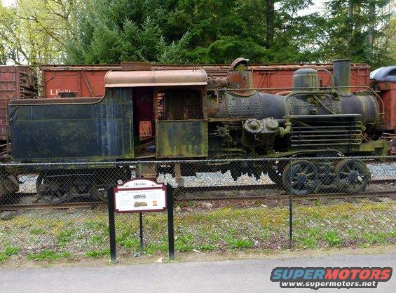 Old steam locomotive with weathered paint, next to a red train car