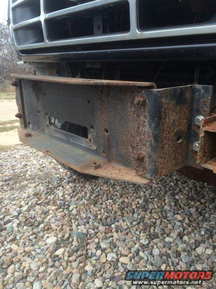 Rusted metal bumper bracket with visible bolts and a rectangular cutout