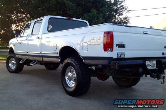 White 1997 Ford F-350 pickup truck with crew cab and lifted suspension, seen from the rear quarter angle