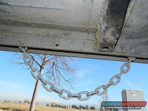 Underside of a vehicle with a chain attached, showing a tree and sky in the background