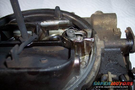 Carburetor with visible oil and grime, showing a spring-loaded mechanism and a wire