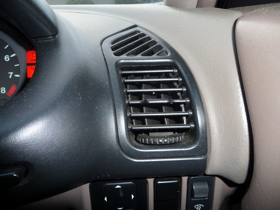 Car interior dashboard vent with beige trim and black grille