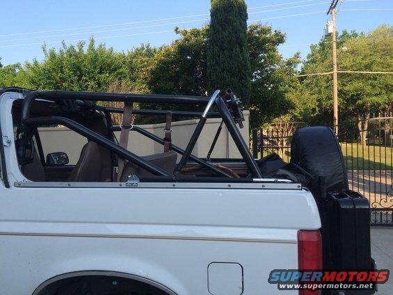 Side view of a white Ford Bronco with a black roll cage installed. Spare tire cover is visible on the rear