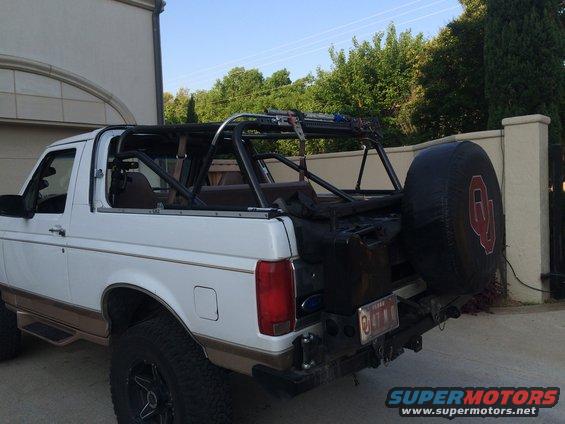White Ford Bronco with brown trim, aftermarket roll cage, and spare tire cover with OU logo, viewed from the rear