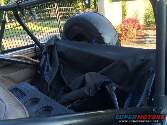Interior view of a vehicle showing a folded soft top, spare tire, and roll cage