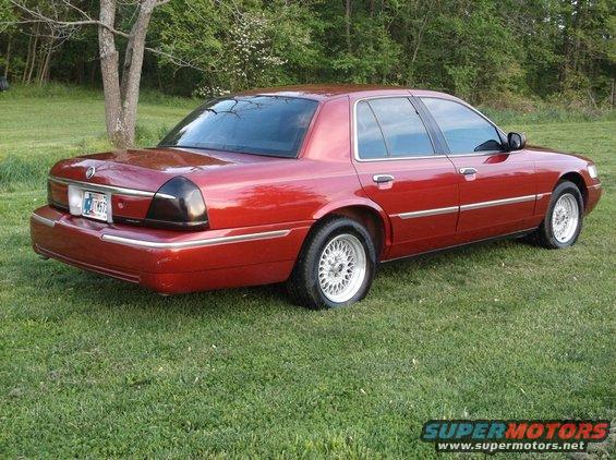 Red sedan parked on grass, rear quarter view. Chrome trim and aftermarket wheels visible