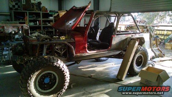 1985 Jeep CJ7 with hood open, doors removed, and roll cage installed, in a garage setting