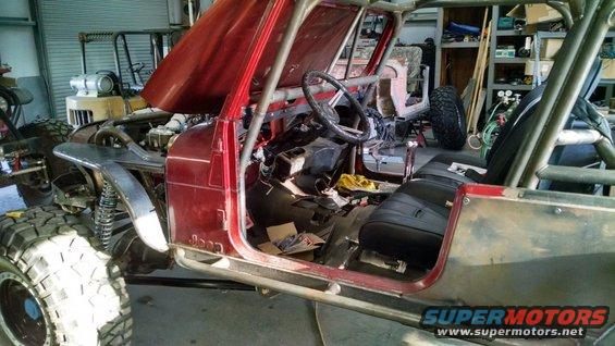 Jeep CJ with hood open, roll cage, and custom fenders. Interior is partially disassembled