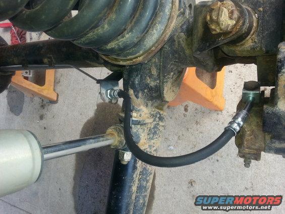 Close-up of a vehicle's front axle, showing suspension components and a brake line. A shock absorber is visible on the left