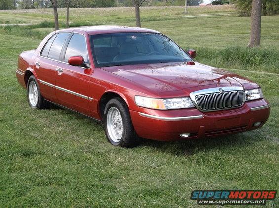 Red sedan parked on grass, front 3/4 view. Chrome grille and trim. Wire wheels
