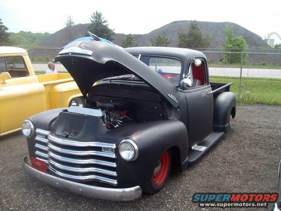 Black pickup truck, front view, hood open, red wheels