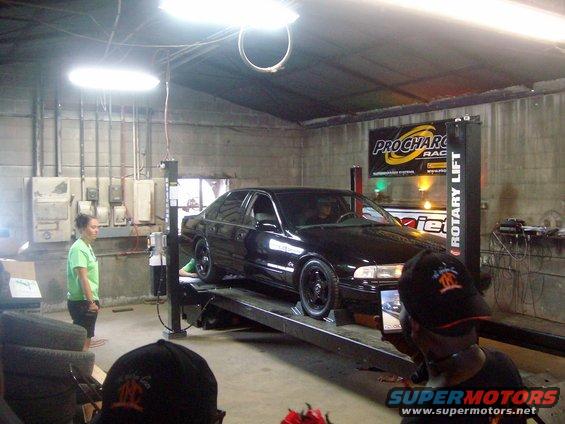 Black sedan on a rotary lift in a garage with people watching