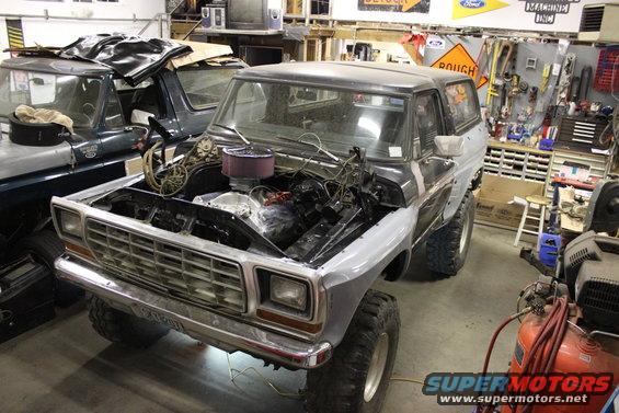 Gray and black Ford Bronco in a garage, hood open, engine exposed, front view